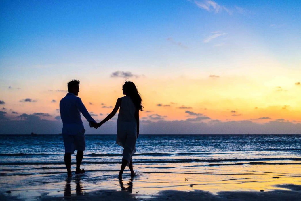 man and woman holding hands walking on seashore du